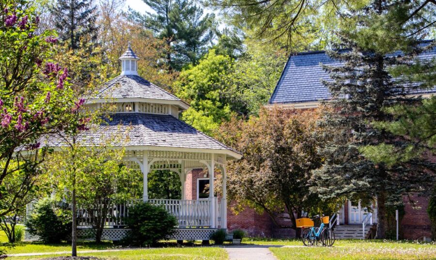 Campus gazebo on a summer day with a blue bicycle on the side and the edge of a red brick building behind.