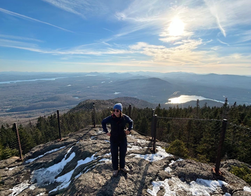 A photo of a young woman in front of a fence on Mont Orford, showing off the scenery, being one of the best landscapes in our region.