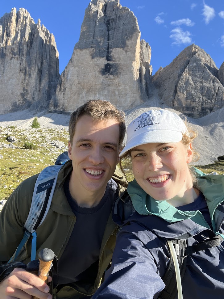 Couple posing for a selfie in hiking gear with a mountain in the back.