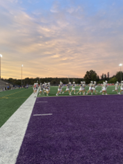 Purple football field with players training under a sunset.