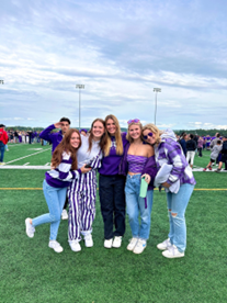 Girls dressed in purple posing in front of the fields at a football game.