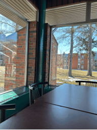  A brown table with two chairs, overlooking a large window with Bishop’s University residence buildings in the background.